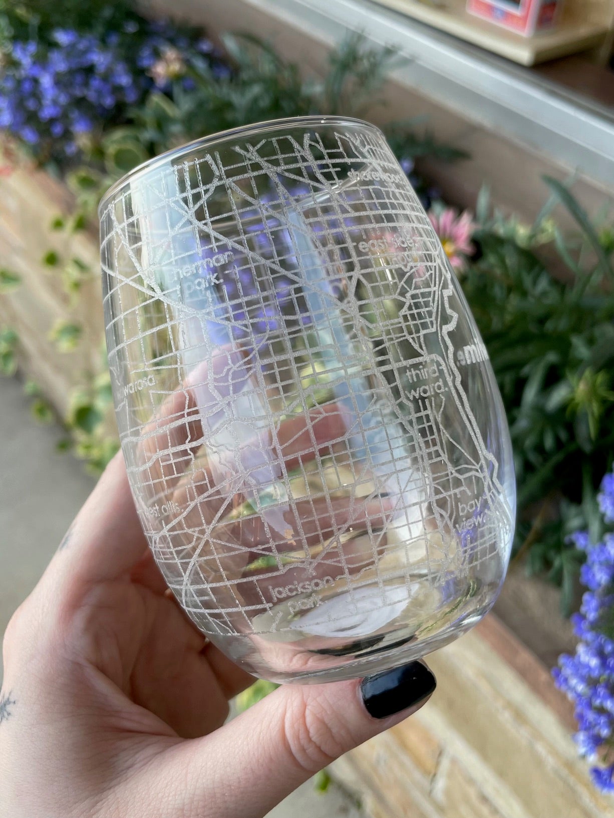 Hand holding a transparent glass with a map design against a blurred floral background